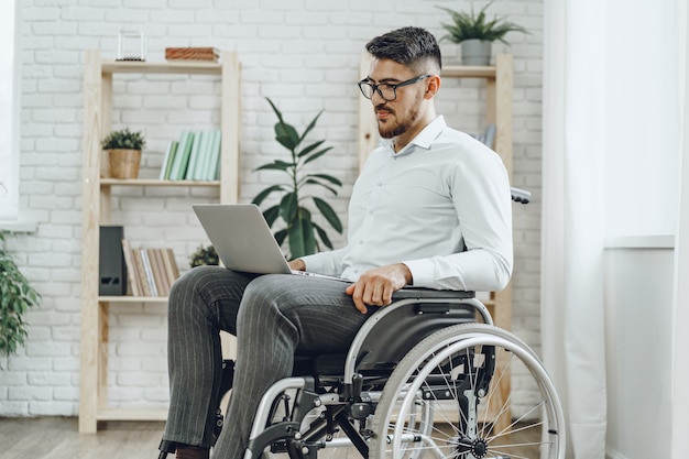 Businessman sitting in wheelchair and using laptop at home