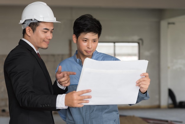 Businessman smiling with engineer and looking blueprint at construction site