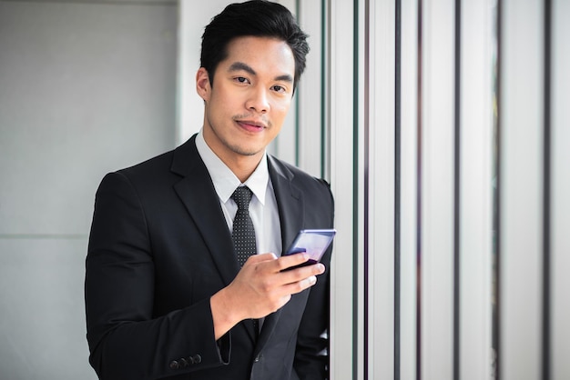 Businessman standing contemplating while use mobile phone and look to camera