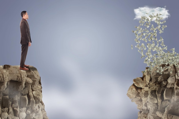 Businessman standing on the edge of mountain looking rain of money on the other side