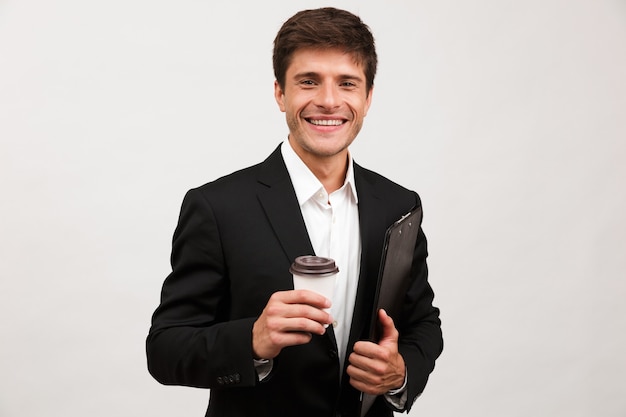 Businessman standing isolated holding clipboard drinking coffee.