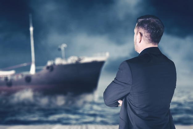 Businessman standing looking at ship sailing in high wind