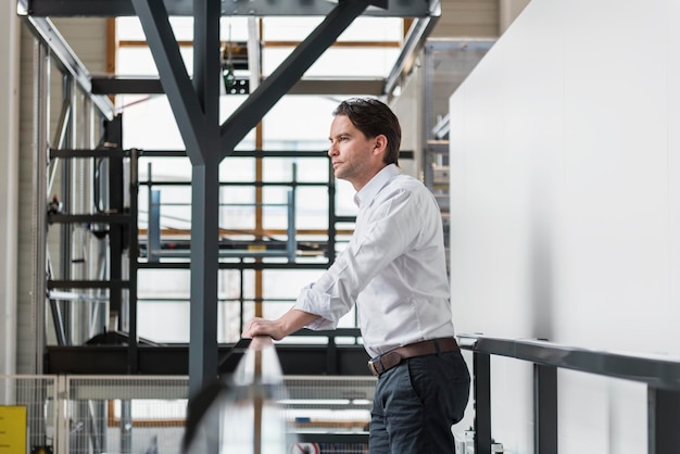 Businessman standing at railing in factory thinking