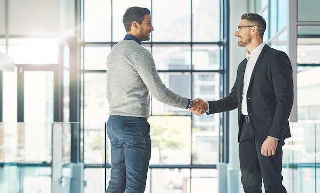 Businessman standing smiling and with a handshake greets a colleague in an office Executive meets client or partner and shakes hands Two happy professionals agree on a successful business project