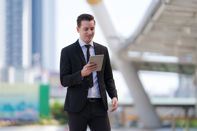 Businessman standing with using a digital tablet in standing in front of modern office buildings