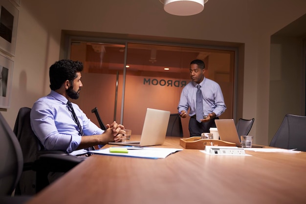 Businessman stands talking to work colleague late in office