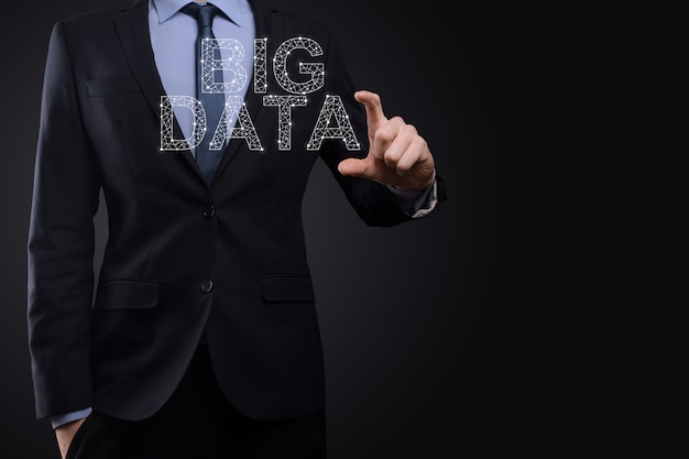 Businessman in a suit on a dark background holds the inscription BIG DATA. Storage Network Online Server Concept.Social network or business analytics representation.