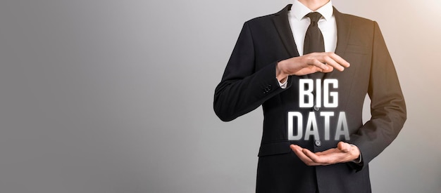 Businessman in a suit on a dark background holds the inscription BIG DATA. Storage Network Online Server Concept.Social network or business analytics representation