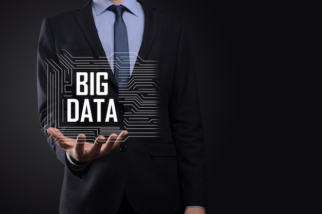 Businessman in a suit on a dark background holds the inscription BIG DATA. Storage Network Online Server Concept.Social network or business analytics representation.