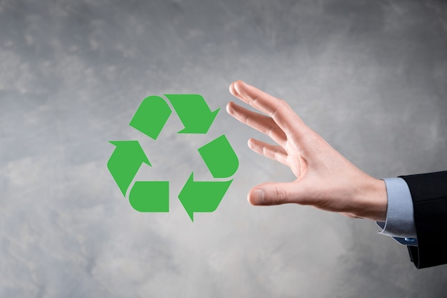 Businessman in suit over dark background holds an recycling icon, sign in his hands. Ecology, environment and conservation concept. Neon red blue light.