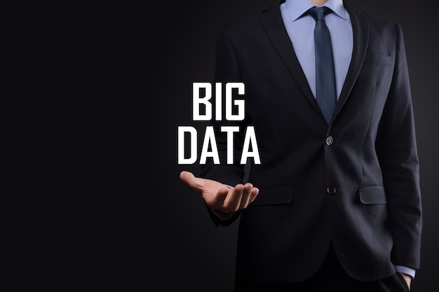 Businessman in a suit on a dark wall holds the inscription BIG DATA. Storage Network Online Server Concept.Social network or business analytics representation.