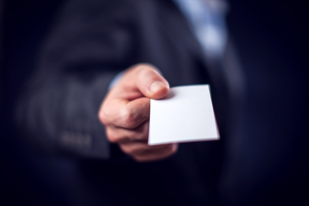 Businessman in suit holding in hand business card in front of black background