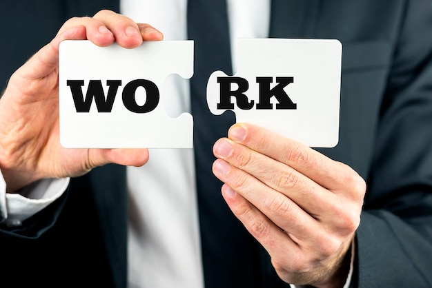 Businessman in a suit holding puzzle pieces with the word Work spread over the two sections.