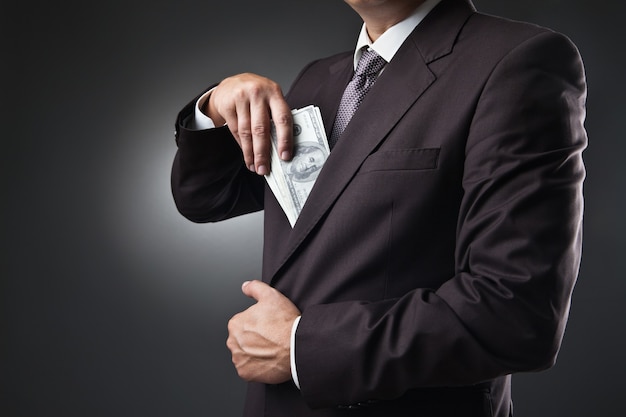 Businessman in suit putting money in his pocket on dark background