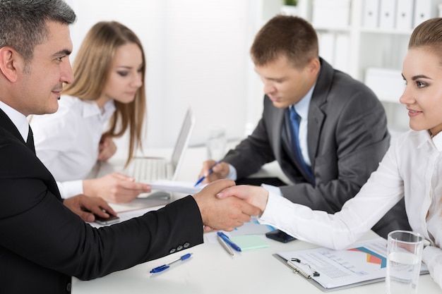 Businessman in suit shaking woman's hand with their colleagues. Partners made deal and sealed it with handclasp. Formal greeting gesture