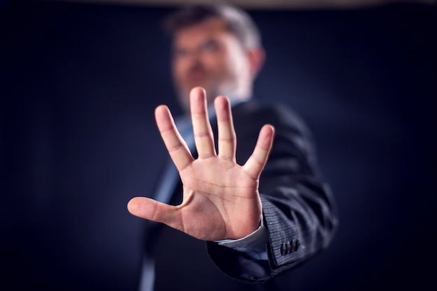 Businessman in suit showing stop sign with hands in front of black background