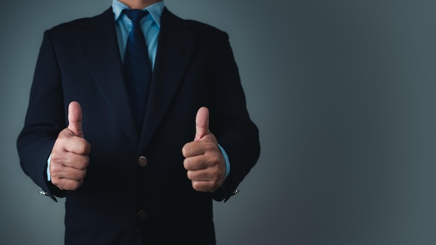 Photo a businessman in a suit stands with his arms crossed and thumbs up on a dark background