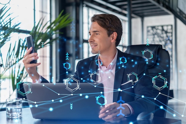 Businessman in suit using smart phone to optimize development by implying new technologies in business process Interconnections and hi tech hologram over modern panoramic office background