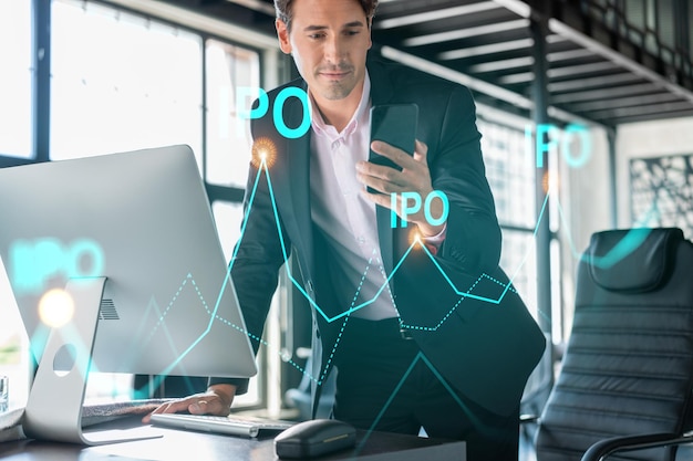 Businessman in suit using smart phone to optimize IPO strategy at corporate finance Chart hologram over modern panoramic office background