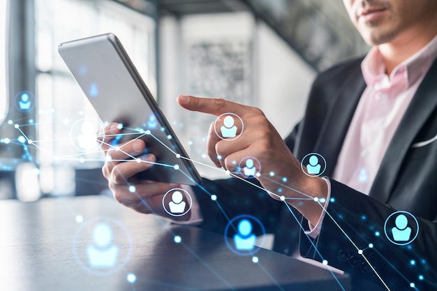 Businessman in suit using tablet device to check new candidates for international business consulting HR social media icons over modern panoramic office background