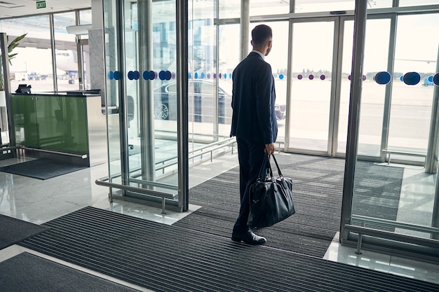 Businessman in a suit walking through entrance hall with a leather suitcase in his hand