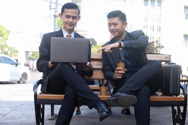 Businessman in suit working on laptop outdoor showing report to boss, sitting outside the office.