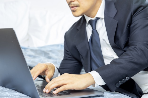 Businessman in suit working on laptop while sitting on the bed, work from home concept.