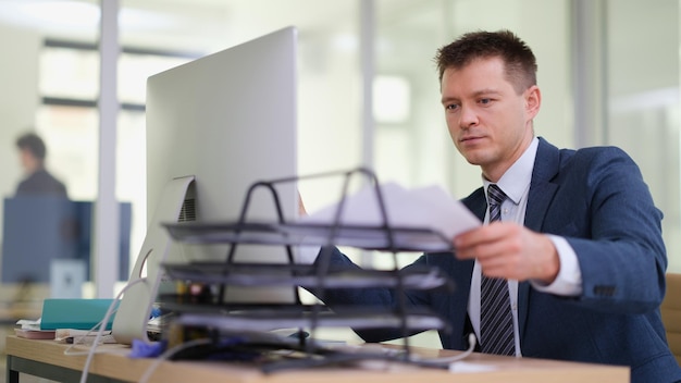 Businessman taking out paper from tray on desk in office