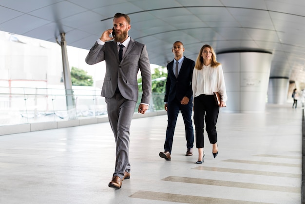 Businessman talking on a phone and business people walking behind him