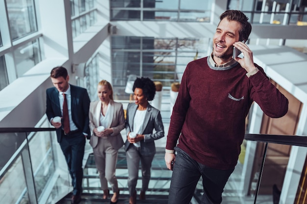 Businessman talking on the phone while his coworkers drinking coffee behind him