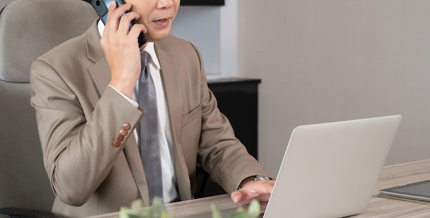 Businessman talking on smartphone and working on laptop computer at office desk