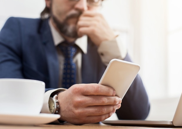 Businessman texting on smartphone, closeup. Pensive SEO at working place