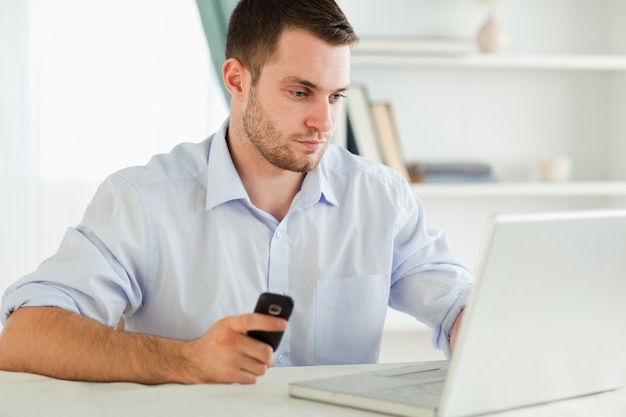 Businessman typing on his laptop while holding cellphone