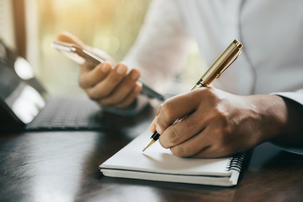 Businessman use a smartphone and laptop computer and take notes in the notebook at the office desk in the morning