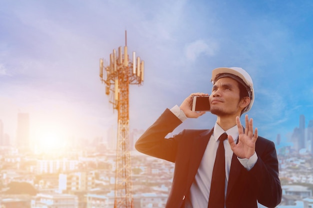 Businessman using cellphone with blurred image of cityscape and telecommunication tower at sunrise