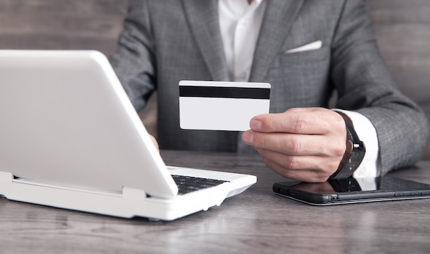 Businessman using laptop computer and holding credit card.