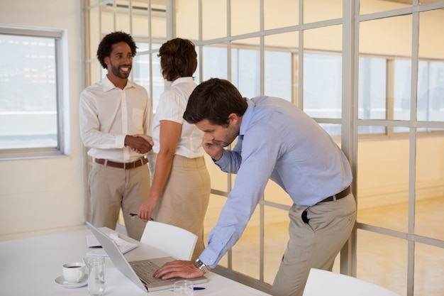 Businessman using laptop with colleagues shaking hands in background