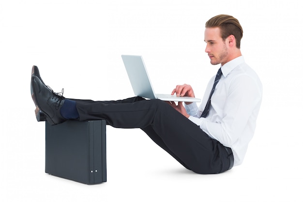 Businessman using laptop with feet up on briefcase