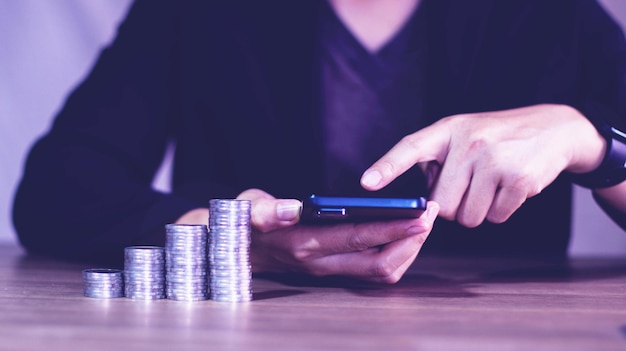 Businessman using mobile searching for investmentinvestment decisionsStacks of coins on table