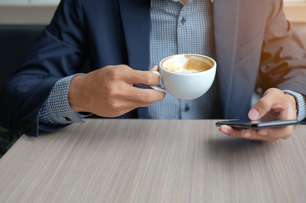 Businessman using smart phone and drinking hot coffee in office