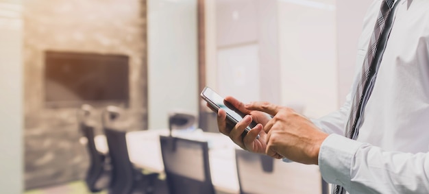 Businessman using smart phone in meeting room interior background and copy space.Concept of workplace using technology