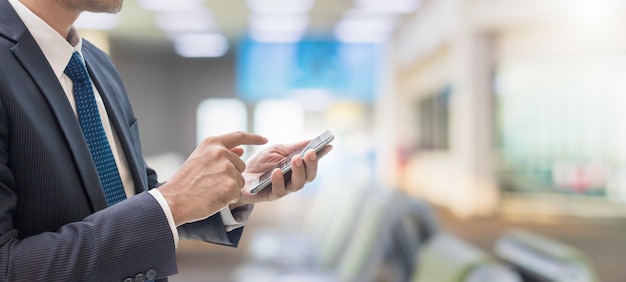 Businessman using smartphone in Airport terminal background with copy spaceConcept of people working online with technology