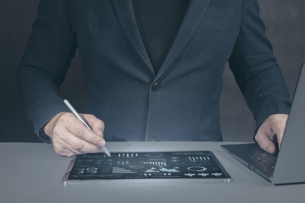 Businessman using tablet analyzing sales data and economic Man in suit works with tablet and laptop with modern interface manages business processes