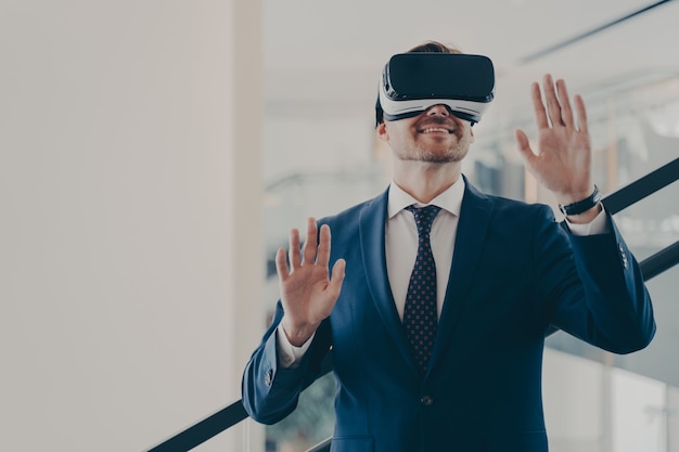 Businessman in virtual reality glasses standing on stairs in office and gesturing