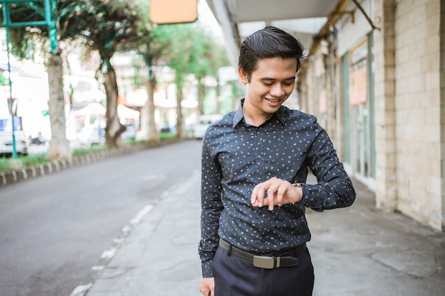 Businessman walking trough sidewalk smiling looking at his wrist watch