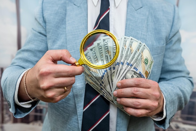 Businessman wear blue suit looking with magnifying glass on dollar bills in office