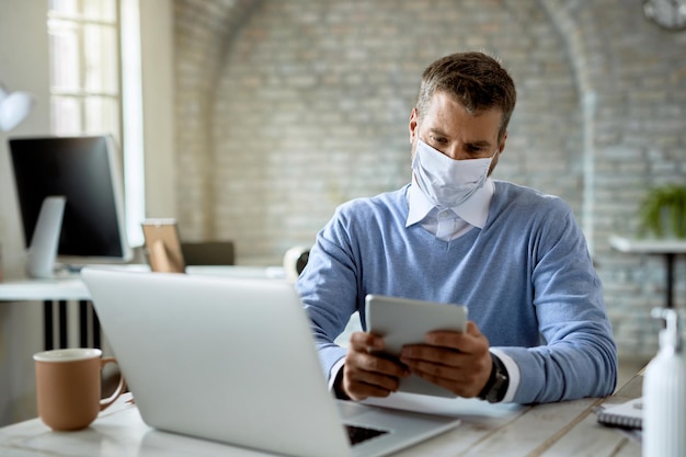 Businessman wearing protective face mask while using touchpad and working in the office