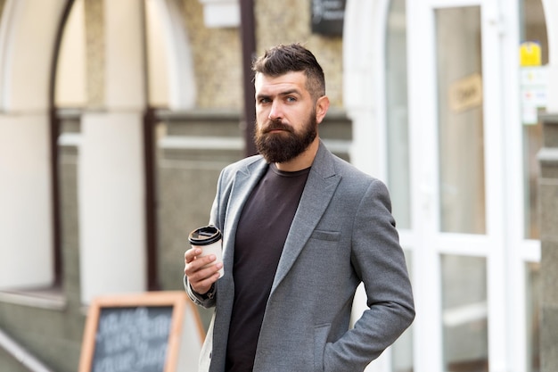 Businessman well groomed appearance enjoy coffee break out of business center Relax and recharge Man bearded hipster drinking coffee paper cup One more sip of coffee Enjoying coffee on the go