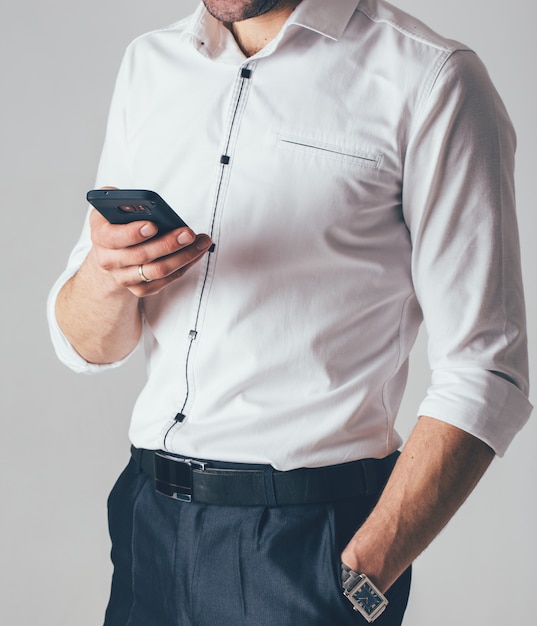 A businessman in a white shirt and black pants holds a phone in his hand in the office. A man wears a wrist watch in his left hand