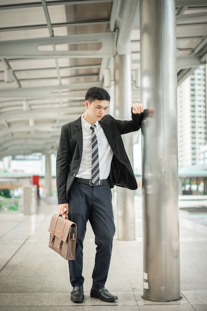 A businessman in a white shirt with neck tie and black suit is holding a handbag.